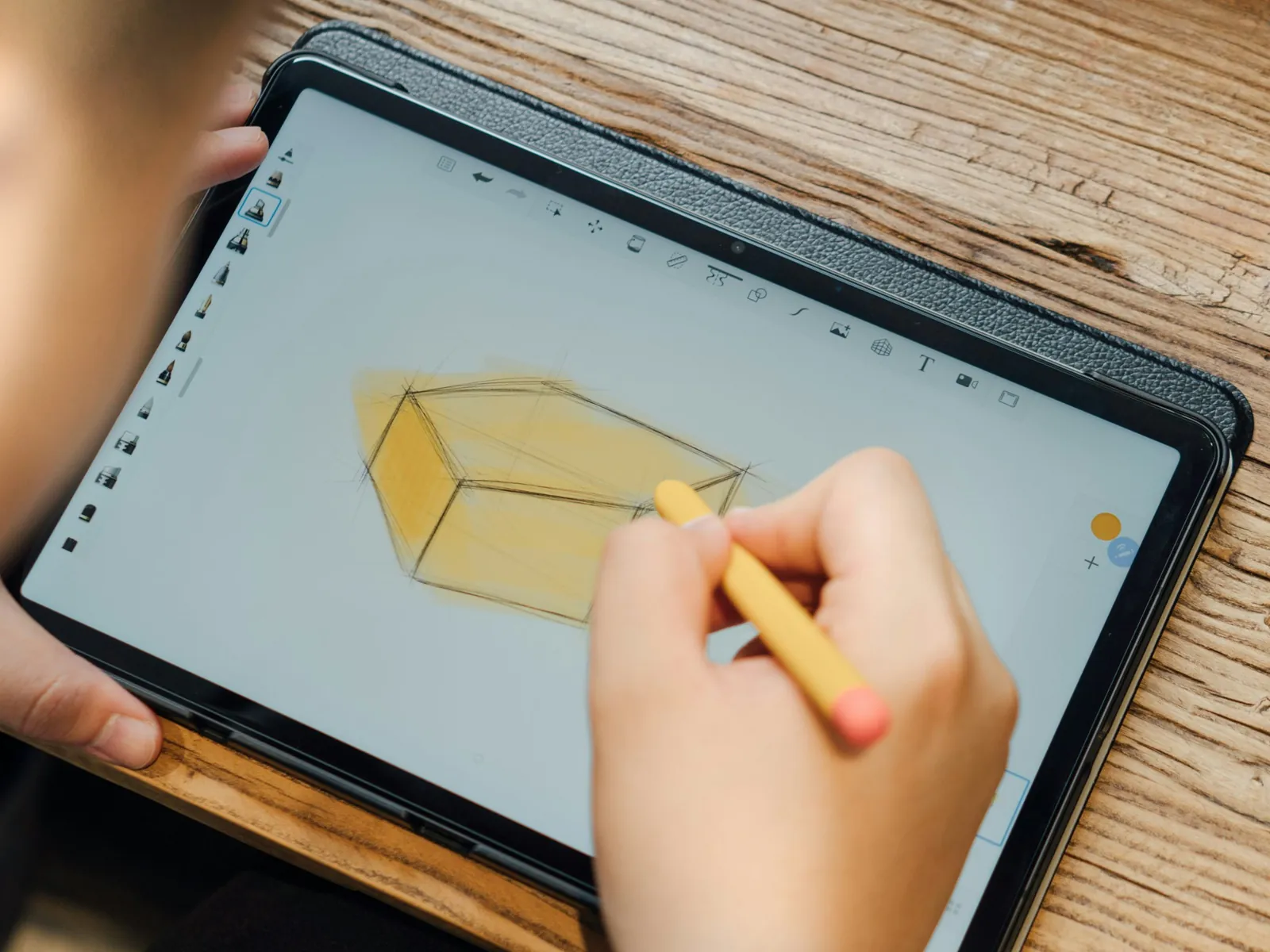 Una persona boceta en una tableta la perspectiva de un objeto, con trazos de construcción y una mancha de color amarilla